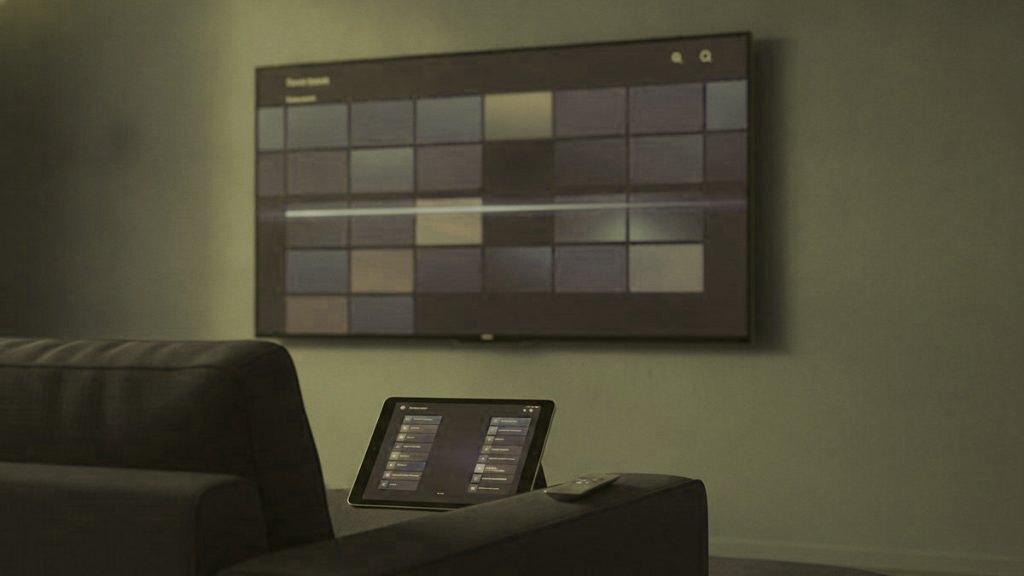 A TV showing a programme guide grid with a tablet and phone showing channel lists on a sofa