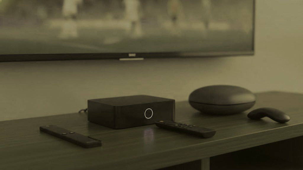 A streaming stick, a set-top box and a round streaming box with their remotes on a TV console