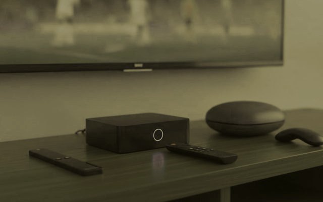 A streaming stick, a set-top box and a round streaming box with their remotes on a TV console
