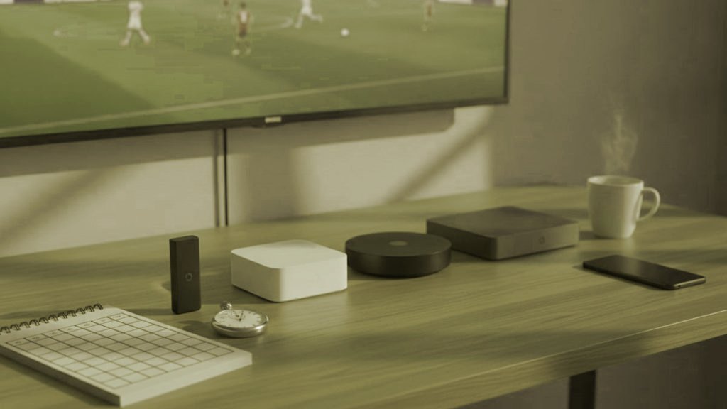 Five streaming devices, a notebook scoring grid and a stopwatch in front of a TV showing a football match