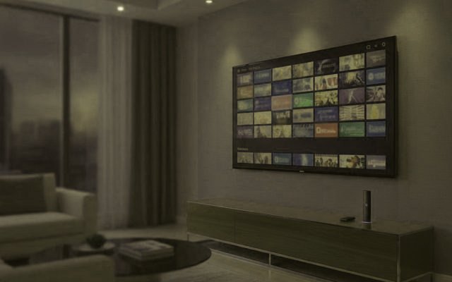 A living-room TV showing an IPTV channel guide with a streaming stick on the console